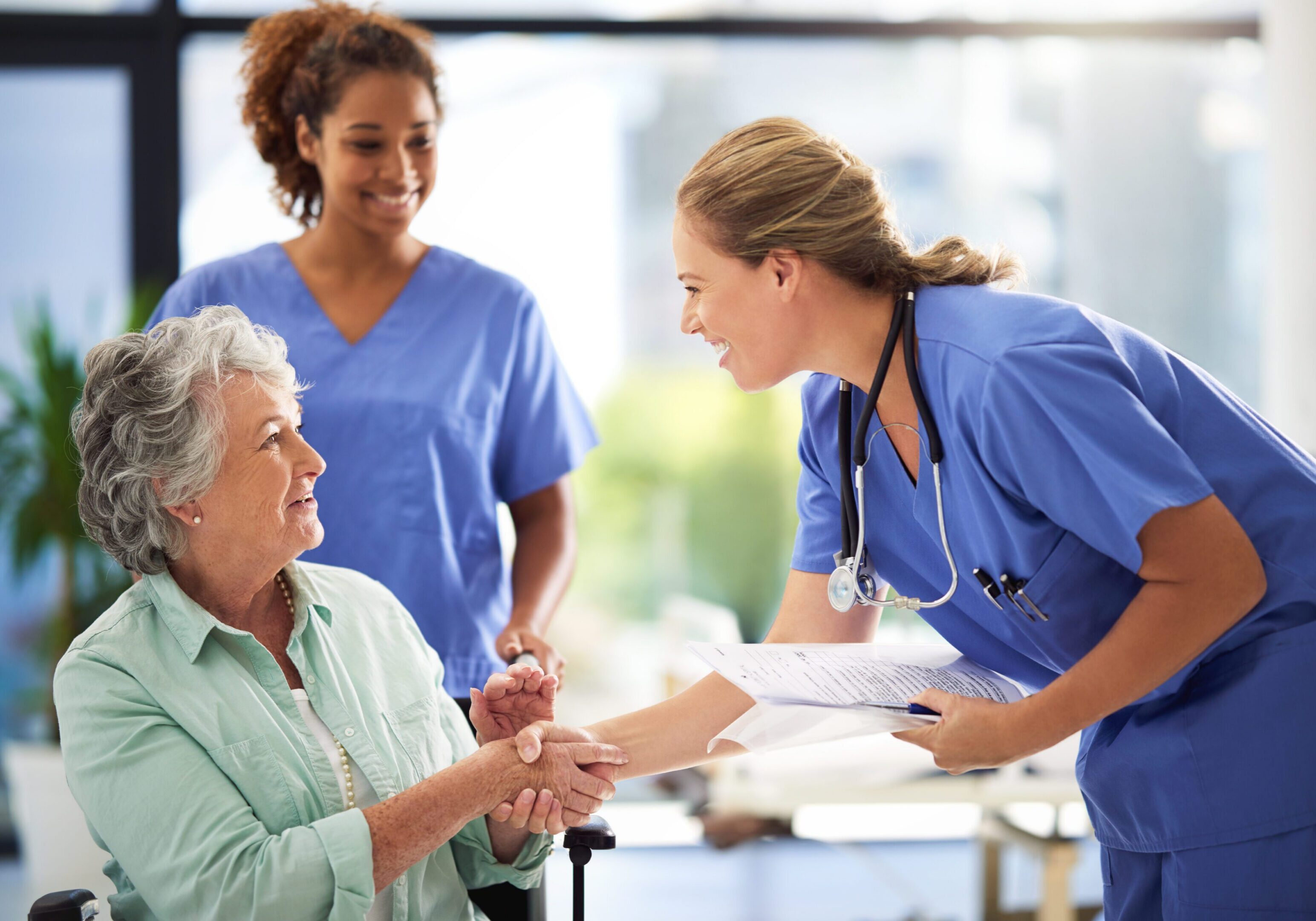 Shot of a doctor holding medical records and shaking hands with a smiling senior woman sitting in a wheelchair
